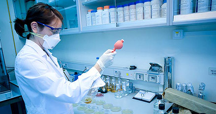Analista con cubrebocas sostiene una perilla de pipeteo junto a cajas de Petri en el laboratorio