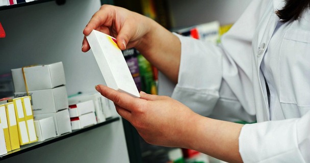 Manos con bata blanca toman una caja de medicamento de un anaquel de farmacia