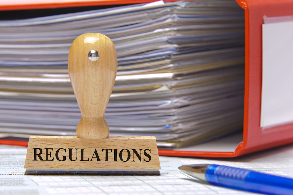 Sello de madera con la palabra REGULATIONS frente a una carpeta roja repleta de documentos