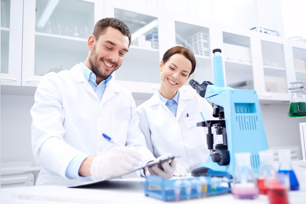 Dos especialistas con bata blanca revisan notas junto a un microscopio en un laboratorio