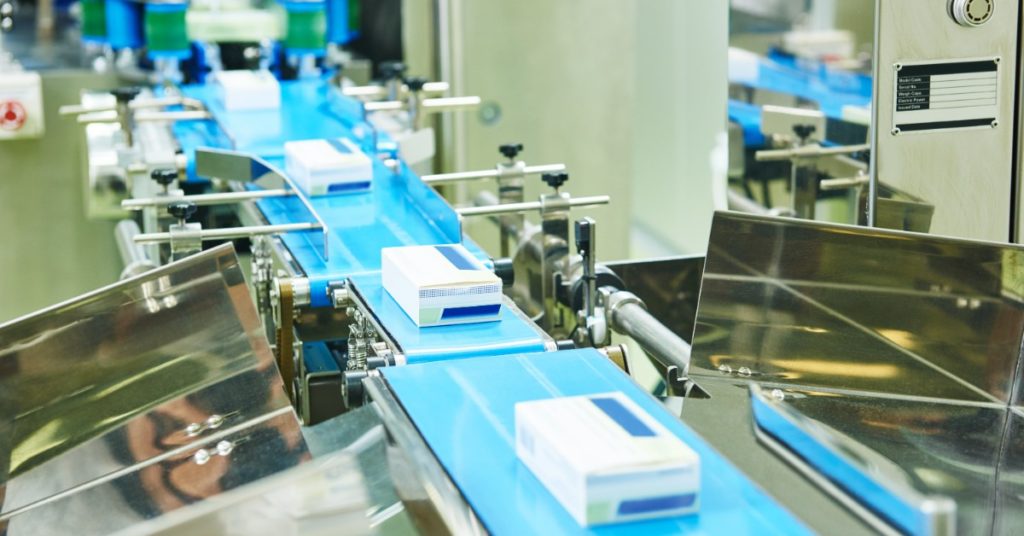 Cajas de medicamento avanzando sobre una banda transportadora azul en una línea de acondicionamiento