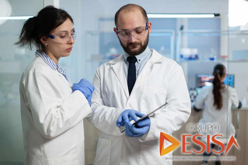 Dos especialistas con bata y lentes de seguridad revisan datos en una tableta dentro de un laboratorio