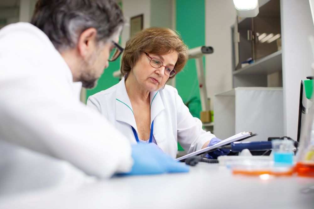 Dos profesionales con bata de laboratorio revisan documentos en un portapapeles